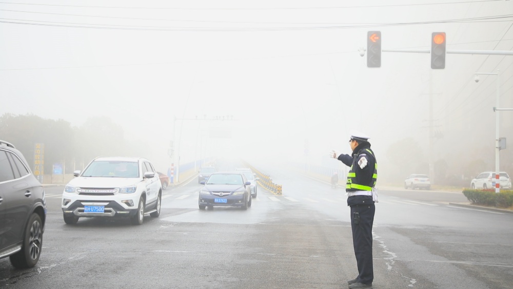 圖為執勤民警正在大霧中指揮過往車輛有序通行.jpg